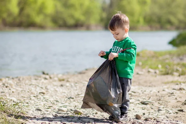 Ahorrar concepto de medio ambiente, un niño recogiendo basura y botellas de plástico en la playa para verter en la basura. — Foto de Stock