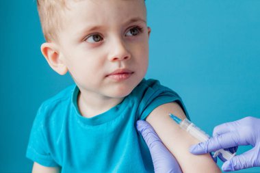 Aşılama konsepti. Mavi arka planda sevimli küçük çocuk aşık kadın doktor, çekim