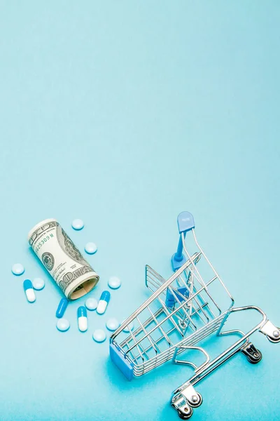 Dollars, pillen en winkelwagentje op een blauwe achtergrond. Apotheek — Stockfoto