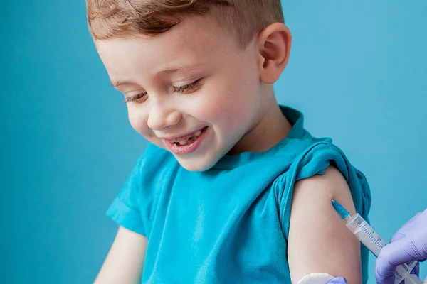 Vaccinatie concept. Vrouwelijke arts vaccineren schattige kleine jongen op blauwe achtergrond, close-up — Stockfoto