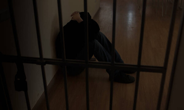 The prisoner behind the bars.Hold with hands on the grids in desperation