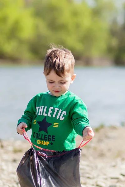 Spara miljö koncept, en liten pojke samla skräp och plastflaskor på stranden för att dumpas i papperskorgen. — Stockfoto