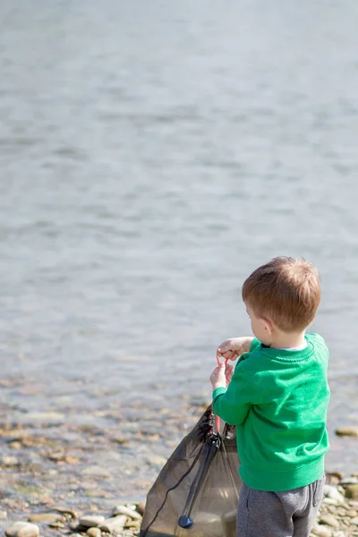 Save Environment Konzept, ein kleiner Junge sammelt Müll und Plastikflaschen am Strand, um sie in den Müll zu werfen. — Stockfoto