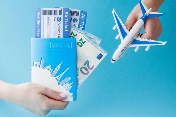 Paspoort, euro, vliegtuig en lucht kaartje in vrouwenhand op een blauwe achtergrond. Reis concept, kopieerruimte — Stockfoto