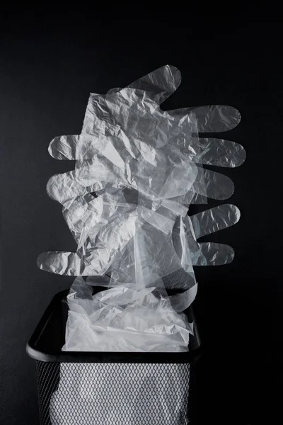 Bolsa de plástico con asas, guantes en la papelera sobre un fondo negro — Foto de Stock