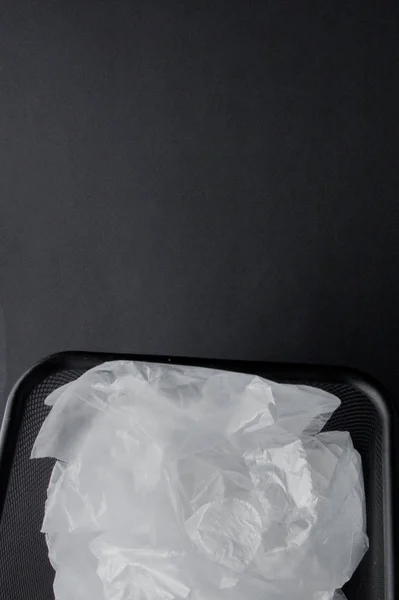 Bolsa de plástico con asas, guantes en la papelera sobre un fondo negro — Foto de Stock