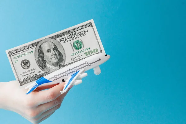 Vliegtuig en dollars in vrouw hand op een blauwe achtergrond. Reizen — Stockfoto