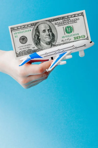 Vliegtuig en dollars in vrouw hand op een blauwe achtergrond. Reizen — Stockfoto