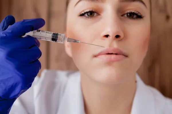 Dokter in handschoenen geven vrouw botox injecties in de lippen, op roze achtergrond — Stockfoto