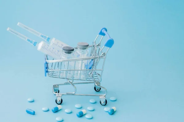 Pills and medical injection in shopping trolley on blue backgrou