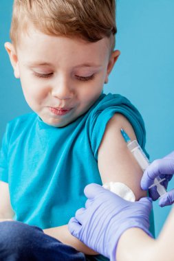 Aşılama konsepti. Mavi arka planda sevimli küçük çocuk aşık kadın doktor, çekim