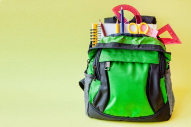 Sarı arka plan müziği üzerinde sırt çantası ve okul Kırtasiye ile kompozisyon