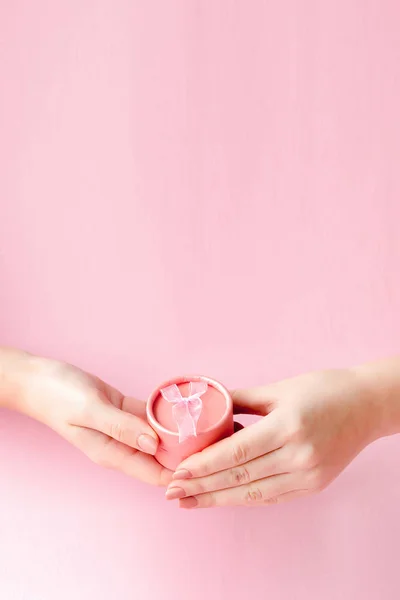 Scatola regalo rotonda rosa nelle mani delle donne su uno sfondo rosa. Concetto festivo per San Valentino, festa della mamma o compleanno — Foto Stock