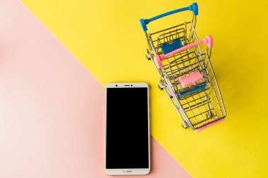 Pastel pembe boş ekran beyaz cep telefonu ve alışveriş arabaları a