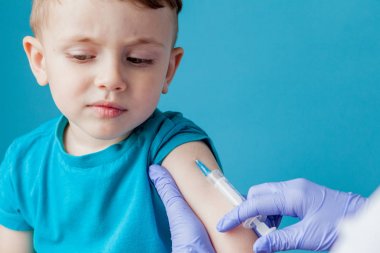 Aşılama konsepti. Mavi arka planda sevimli küçük çocuk aşık kadın doktor, çekim