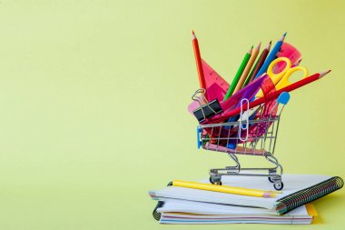 Shopping cart with different stationery on the yellow background clipart