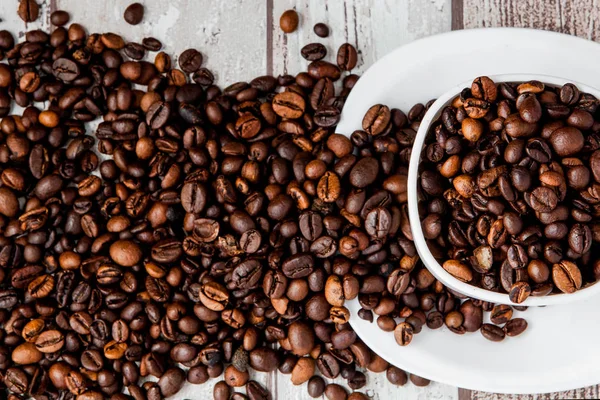 Černou kávu v bílém šálku a kávovou fazoli na světle dřevěném pozadí. Pohled shora, prostor pro text — Stock fotografie