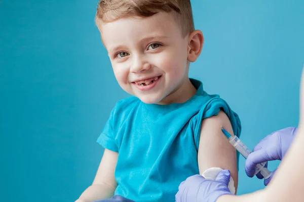 Vaccinatie concept. Vrouwelijke arts vaccineren schattige kleine jongen op blauwe achtergrond, close-up — Stockfoto