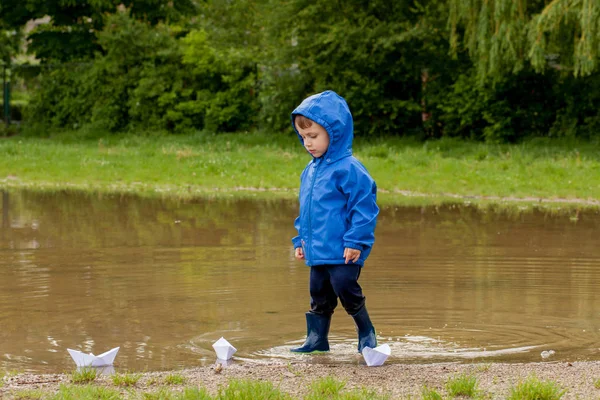Portrait d'un garçon mignon jouant avec un bateau fait main. maternelle garçon voile un bateau jouet par le bord de l'eau dans le parc — Photo