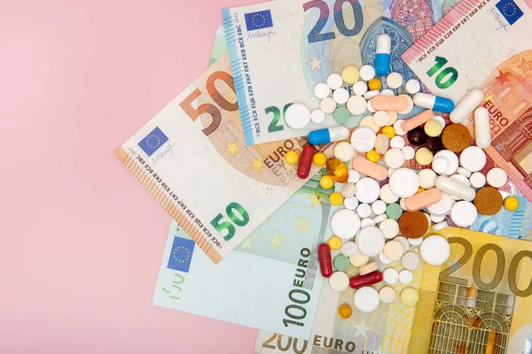 Таблетки и евро на розовом фоне с копировальным местом. Мягкий фокус — стоковое фото