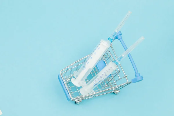 Medical injection in shopping trolley on blue background. Creati
