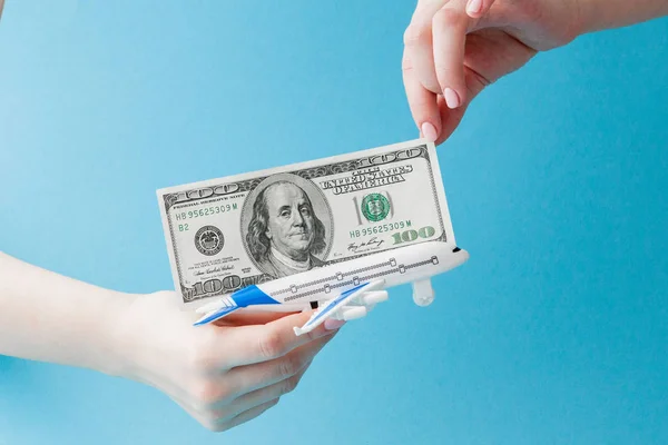 Vliegtuig en dollars in vrouw hand op een blauwe achtergrond. Reis concept, kopieer ruimte — Stockfoto