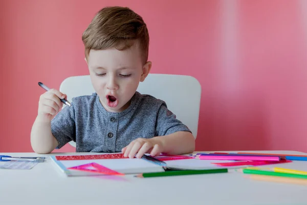 Retrato de menino bonito em casa fazendo lição de casa. Pequena condescendência — Fotografia de Stock