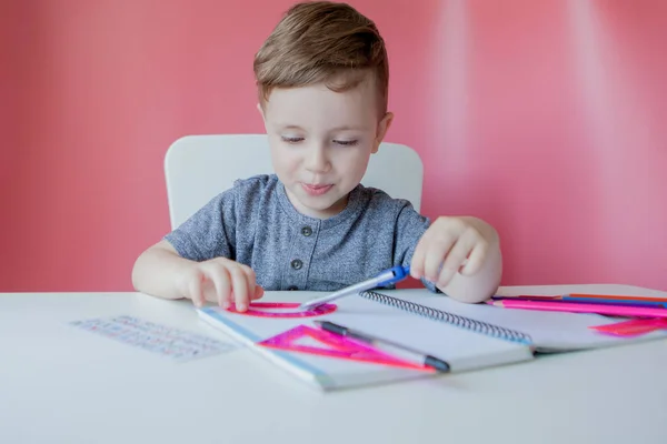 Retrato de menino bonito em casa fazendo lição de casa. Pequena condescendência — Fotografia de Stock