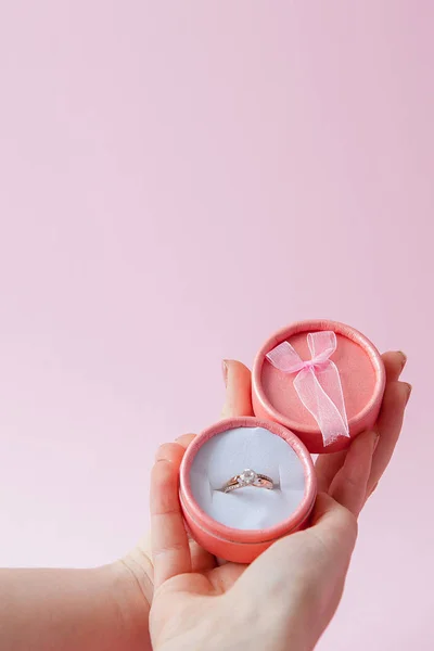 Frau öffnet eine Geschenkschachtel mit Schmuck. Ehering in einer Schachtel in den Händen von Frauen auf rosa Hintergrund — Stockfoto