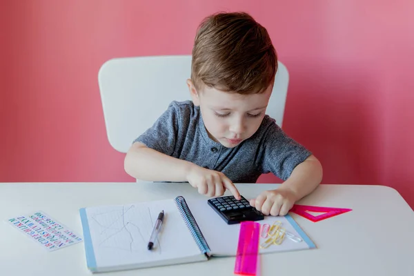 Retrato de menino bonito em casa fazendo lição de casa. Pequena criança concentrada escrevendo com lápis colorido, dentro de casa. Escola primária e educação. Criança aprendendo a escrever letras e números — Fotografia de Stock