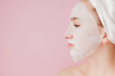 Güzel genç kadın kozmetik doku maske pembe bir arka plan üzerinde bir yüzünde uyguluyor. Sağlık ve güzellik tedavi ve teknoloji kavramı