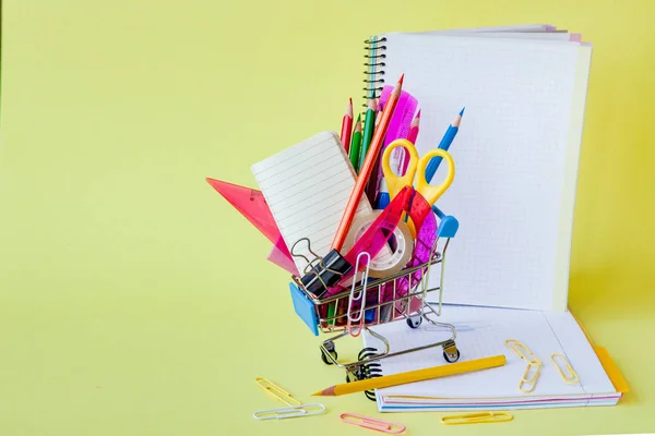 Shopping cart with different stationery on the yellow background — Stock Photo, Image