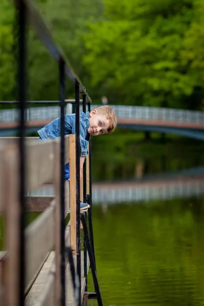 一个小男孩爬上公园里的一座桥栏杆。威胁 — 图库照片