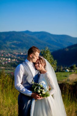 Yeni evliler gülümseme ve diğer her dağın zirvesinde çayır arasında sarıl. Düğün yürüyüş dağlar, nazik duygular çift, Sevgililer günü için fotoğraf ormanda