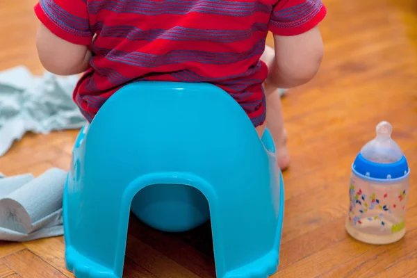 Pequeno bebê sentado no pote da câmara com papel higiênico e chupeta em um fundo marrom — Fotografia de Stock
