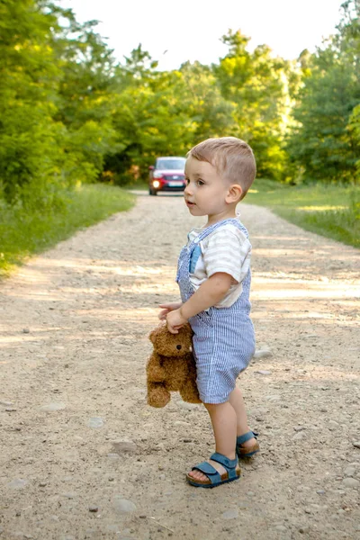 Un niño pequeño en un camino en el bosque. Peligro en la carretera. El niño está en peligro en el camino. —  Fotos de Stock