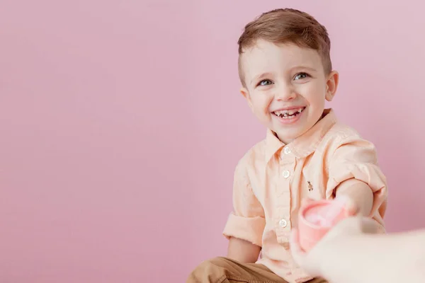 Um rapazinho feliz com um dom. Foto isolada em fundo rosa. Rapaz sorridente segura a caixa de presente. Conceito de feriados e aniversário — Fotografia de Stock