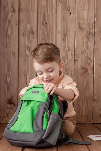 Ahşap arka planda büyük okul çantalı küçük çocuk. — Stok fotoğraf