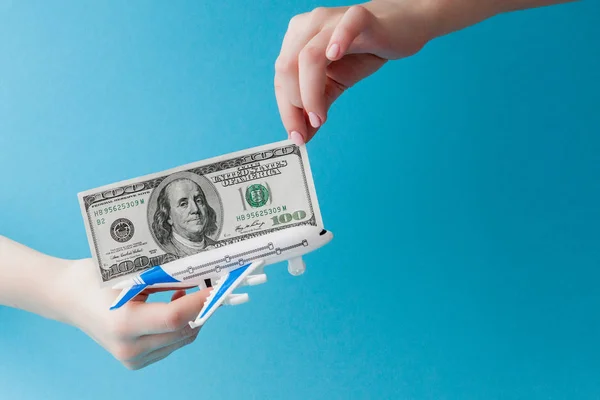 Vliegtuig en dollars in vrouw hand op een blauwe achtergrond. Reis concept, kopieer ruimte — Stockfoto