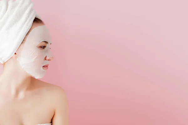 Wanita muda yang cantik menerapkan masker jaringan kosmetik pada wajah dengan latar belakang merah muda. Kesehatan dan kecantikan pengobatan dan konsep teknologi — Stok Foto