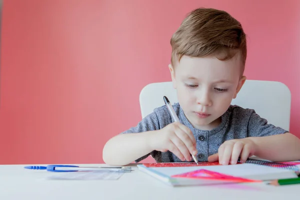 Портрет симпатичного хлопчика вдома, який робить домашнє завдання. Маленька концентрована дитина пише з барвистим олівцем, в приміщенні. Початкова школа та освіта. Малюк вчиться писати літери та цифри — стокове фото