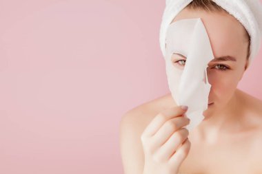 Güzel genç kadın kozmetik doku maske pembe bir arka plan üzerinde bir yüzünde uyguluyor. Sağlık ve güzellik tedavi ve teknoloji kavramı