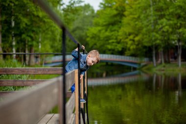 Küçük bir çocuk parktaki bir köprüye tırmanıyor. Boğulma tehdidi. Çocuklar için tehlike