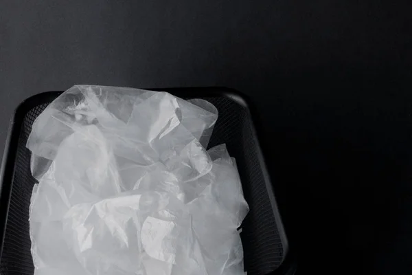 Bolsa de plástico con asas, guantes en el cubo sobre fondo negro. Bolsa de plástico usada para reciclar. Concepto - ecología, contaminación planetaria con polietileno de celofán plástico — Foto de Stock