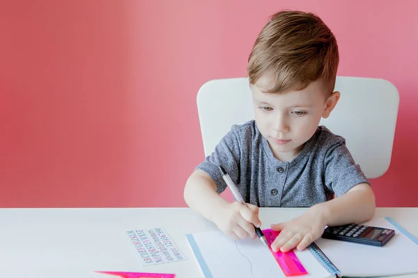 Portret van schattige jongen thuis maken huiswerk. Weinig geconcentreerd kind schrijven met kleurrijke potlood, binnenshuis. Basisschool en onderwijs. Kid Learning schrijven letters en cijfers — Stockfoto