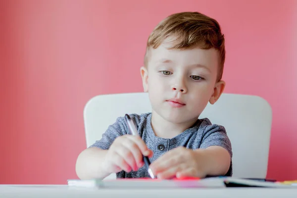 Retrato de menino bonito em casa fazendo lição de casa. Pequena criança concentrada escrevendo com lápis colorido, dentro de casa. Escola primária e educação. Criança aprendendo a escrever letras e números — Fotografia de Stock