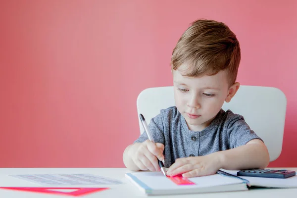 Retrato de niño lindo en casa haciendo tarea. Pequeña escritura infantil concentrada con lápiz de colores, en interiores. Escuela primaria y educación. Niño aprendiendo a escribir letras y números —  Fotos de Stock