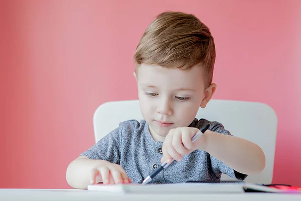 Retrato de niño lindo en casa haciendo tarea. Pequeña escritura infantil concentrada con lápiz de colores, en interiores. Escuela primaria y educación. Niño aprendiendo a escribir letras y números —  Fotos de Stock