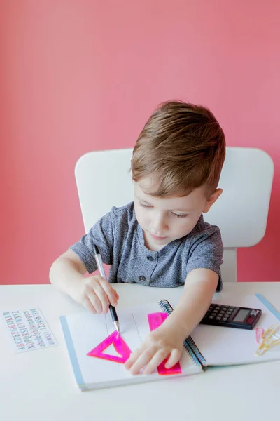 Retrato de menino bonito em casa fazendo lição de casa. Pequena criança concentrada escrevendo com lápis colorido, dentro de casa. Escola primária e educação. Criança aprendendo a escrever letras e números — Fotografia de Stock