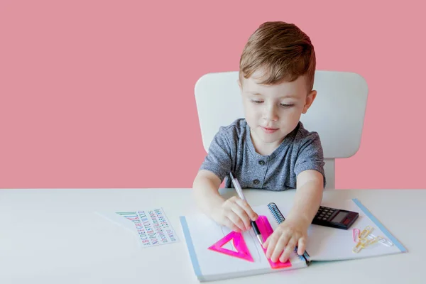 Ritratto di ragazzo carino a casa a fare i compiti. Piccolo bambino concentrato che scrive con matita colorata, in casa. Scuola elementare e istruzione. Kid imparare a scrivere lettere e numeri — Foto Stock